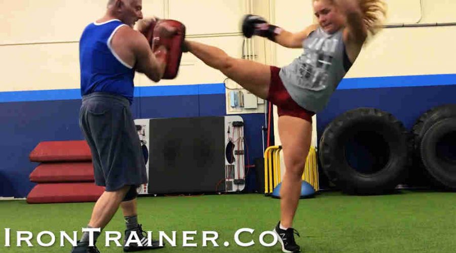 kickboxing coach holding kick pads while client throws a roundhouse kick with pivot on the ball of the foot