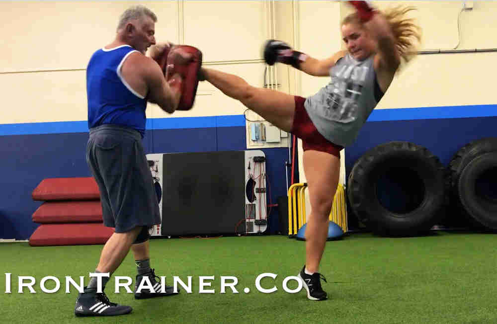 kickboxing coach holding kick pads while client throws a roundhouse kick with pivot on the ball of the foot